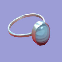 A silver ring with a large, oval cabochon gemstone featuring light blue and white marbled patterns, shown against a solid purple background.